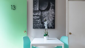 Une pièce avec un mur vert, une porte blanche, une table blanche, deux chaises turquoise et une œuvre d’art en forme de guitare accrochée au mur.