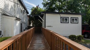 Une terrasse en bois menant à une buanderie, avec un panneau indicateur, le tout entouré d’immeubles d’habitation.