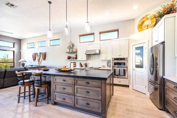 A modern kitchen with a large island, white cabinets, stainless steel appliances, and pendant lighting.