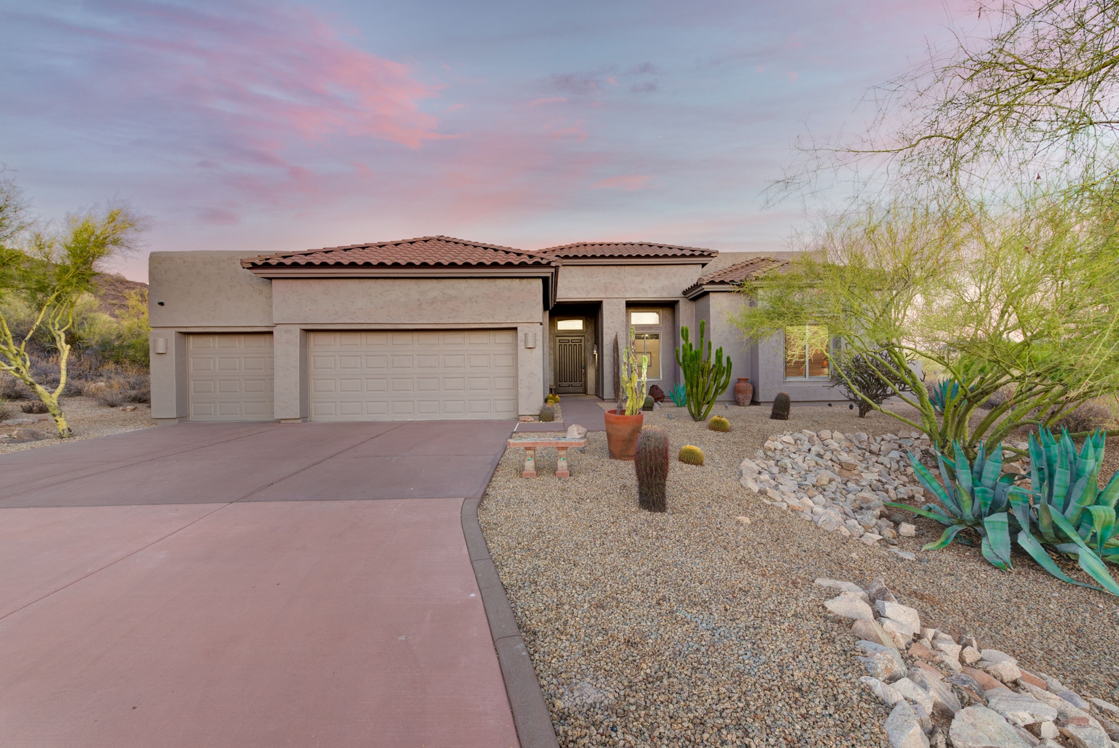 A two-story house with a garage, a driveway, and a landscaped garden with cacti and rocks.