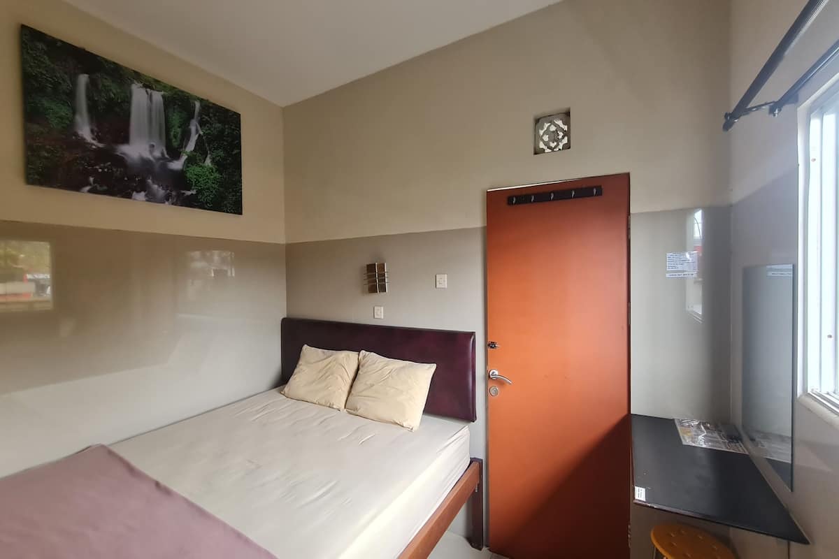 Une chambre à coucher avec un lit, une porte, une petite table, une fenêtre et un tableau accroché au mur.