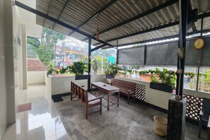 A covered outdoor seating area with a table and benches, potted plants, and a view of a carnival ride. - Capital O 93250 Hotel Tirta Kencana 2 Baturaden (Baturaden)