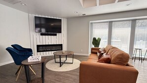 A modern living room with a sofa, a blue chair, a coffee table, and a TV mounted on the wall. - SE Boise Condo • Pool • Parking • Hot Tub+ 2 Private Master Suites (Boise)
