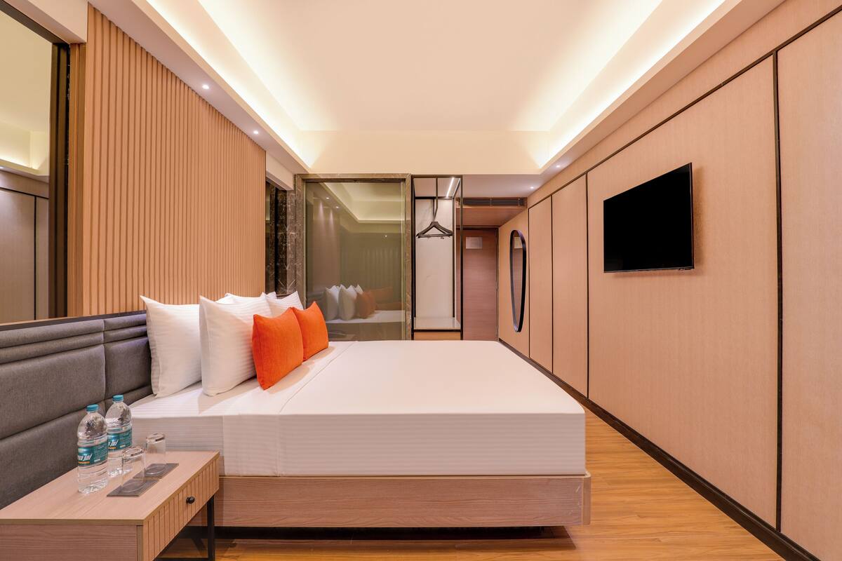 A modern hotel room with a large bed, bedside table, and a TV mounted on the wall.
