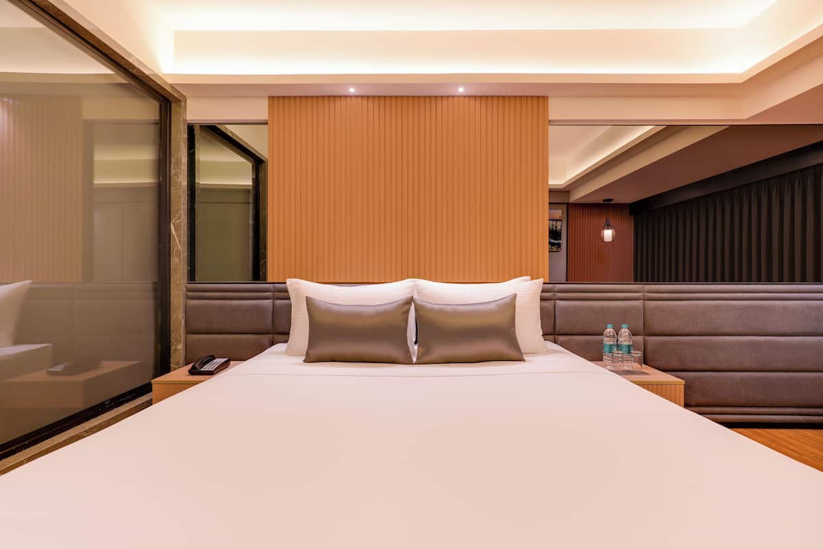 Habitación de hotel con una cama grande, un cabecero de madera, una mesita de noche con un teléfono y vistas a través de una puerta de vidrio.