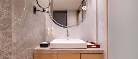 A modern bathroom with a marble sink, wooden vanity, and a round mirror with a light.