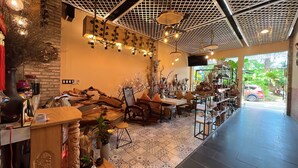 Een gezellig café met rustieke inrichting, waaronder een houten tafel en stoelen, een stenen muur en een plafond met een ruitpatroon.