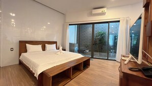 Een moderne slaapkamer met een houten bed, een inbouwkbank, een grote schuifdeur naar een balkon met planten en een aan het plafond bevestigde airconditioning.