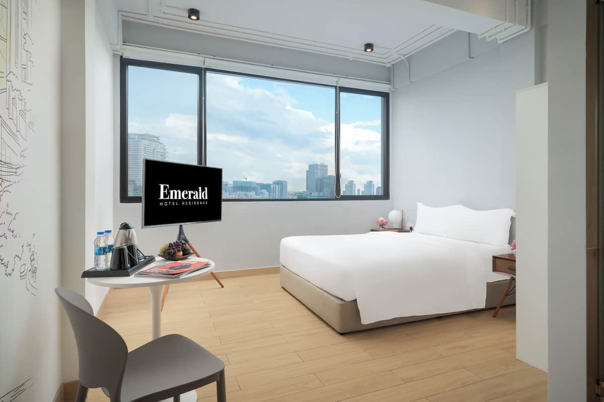 Ein Hotelzimmer mit einem Bett, einem Schreibtisch mit Stuhl, einem Fernseher und einem großen Fenster mit Blick auf die Stadt.