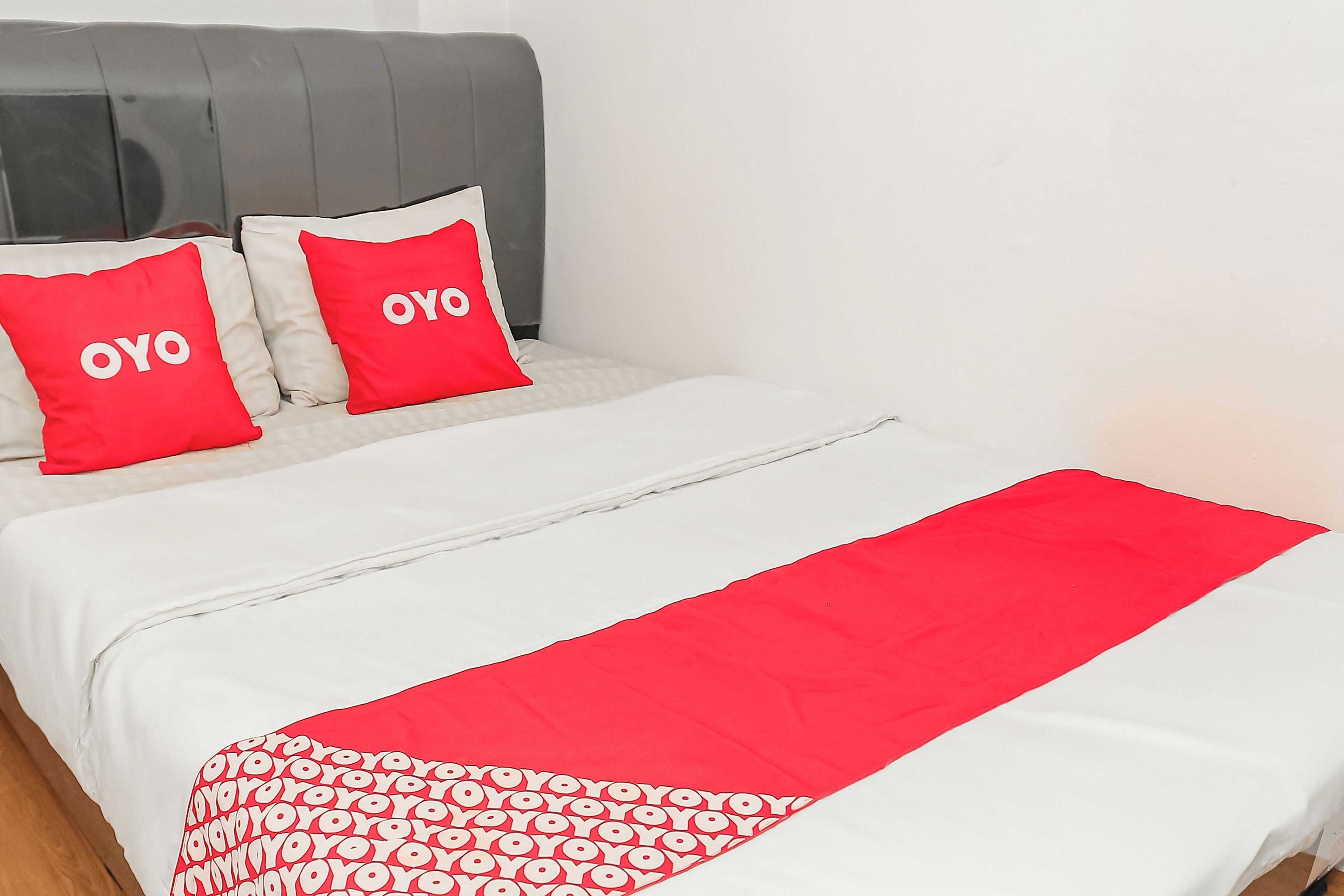 A bed with a white and red bedspread, two pillows with 'OYO' text, and a grey headboard.