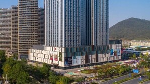 A modern high-rise building with a glass facade, surrounded by other buildings and a hilly landscape. - Ginlan jia hotel Hangzhou Xintiandi (Hangzhou)