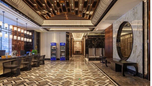 A modern hotel lobby with a geometric patterned floor, a reception desk with chairs, a vending machine, and a large mirror on the wall. - Ginlan jia hotel Hangzhou Xintiandi (Hangzhou)