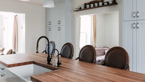 A kitchen with a wooden island, white cabinets, and a dining area with wicker chairs. - Little Louis - A Princely Take on a County Getaway (Prince Edward)