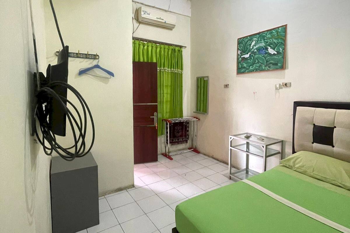 A room with a bed, a small table, a radiator, a green curtain, and a wall-mounted air conditioner.