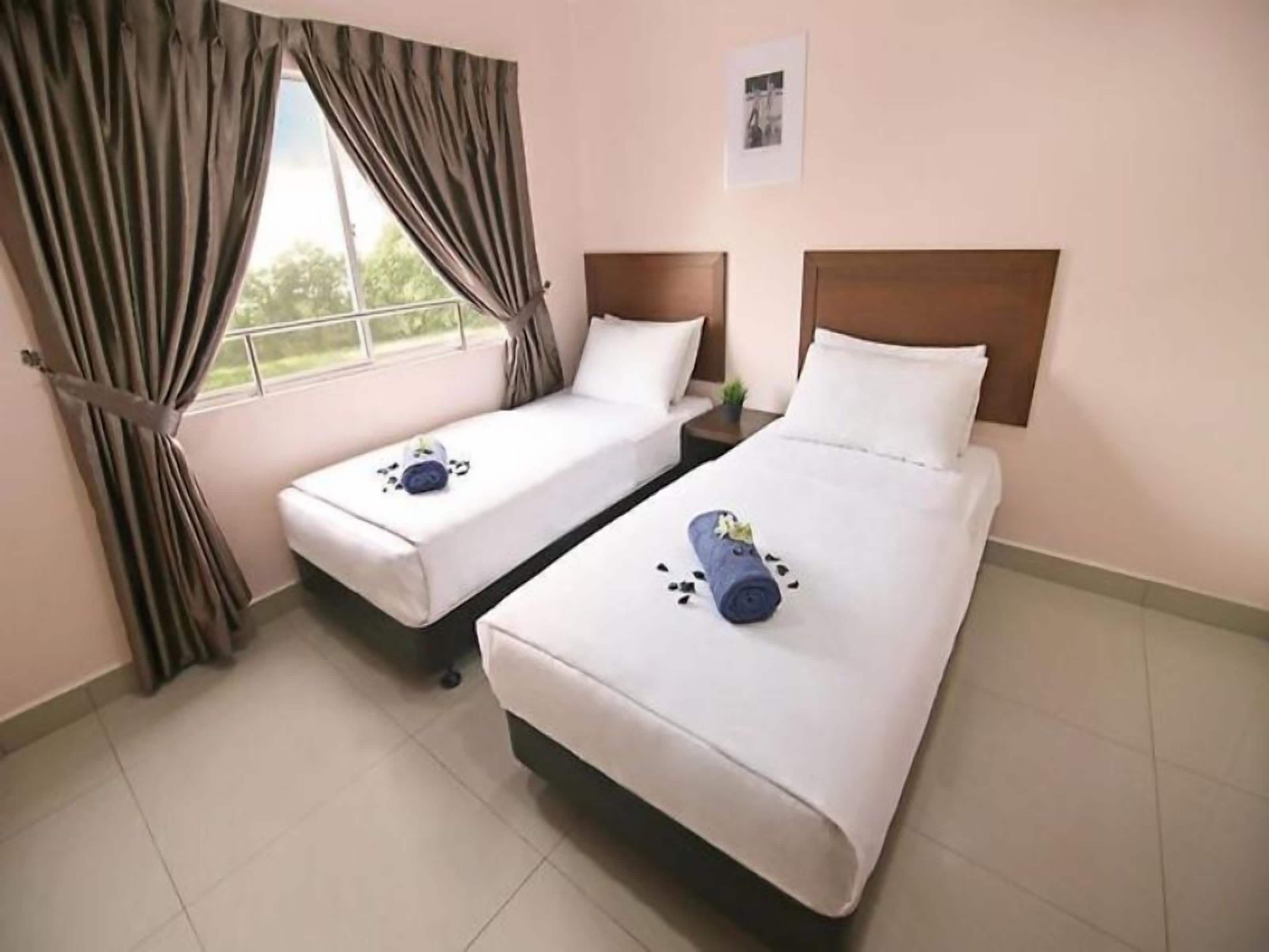 A hotel room with two single beds, a window with curtains, a small bedside table, and a picture on the wall.