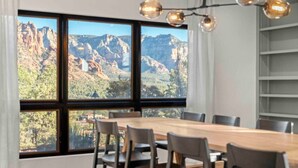 Un comedor con una gran mesa y sillas, vistas a un paisaje montañoso a través de amplios ventanales y una lámpara moderna.