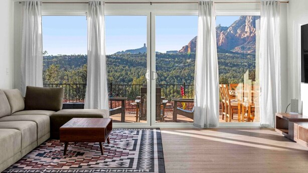 Un salón con un sofá, una mesa de centro y un tapete estampado. Cuenta con grandes puertas correderas de vidrio que dan a un balcón exterior con sillas y una mesa.