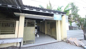 A building entrance with a covered walkway, metal gates, and a bench outside. - OYO 93267 Barokah Rooms Syariah (Praya)