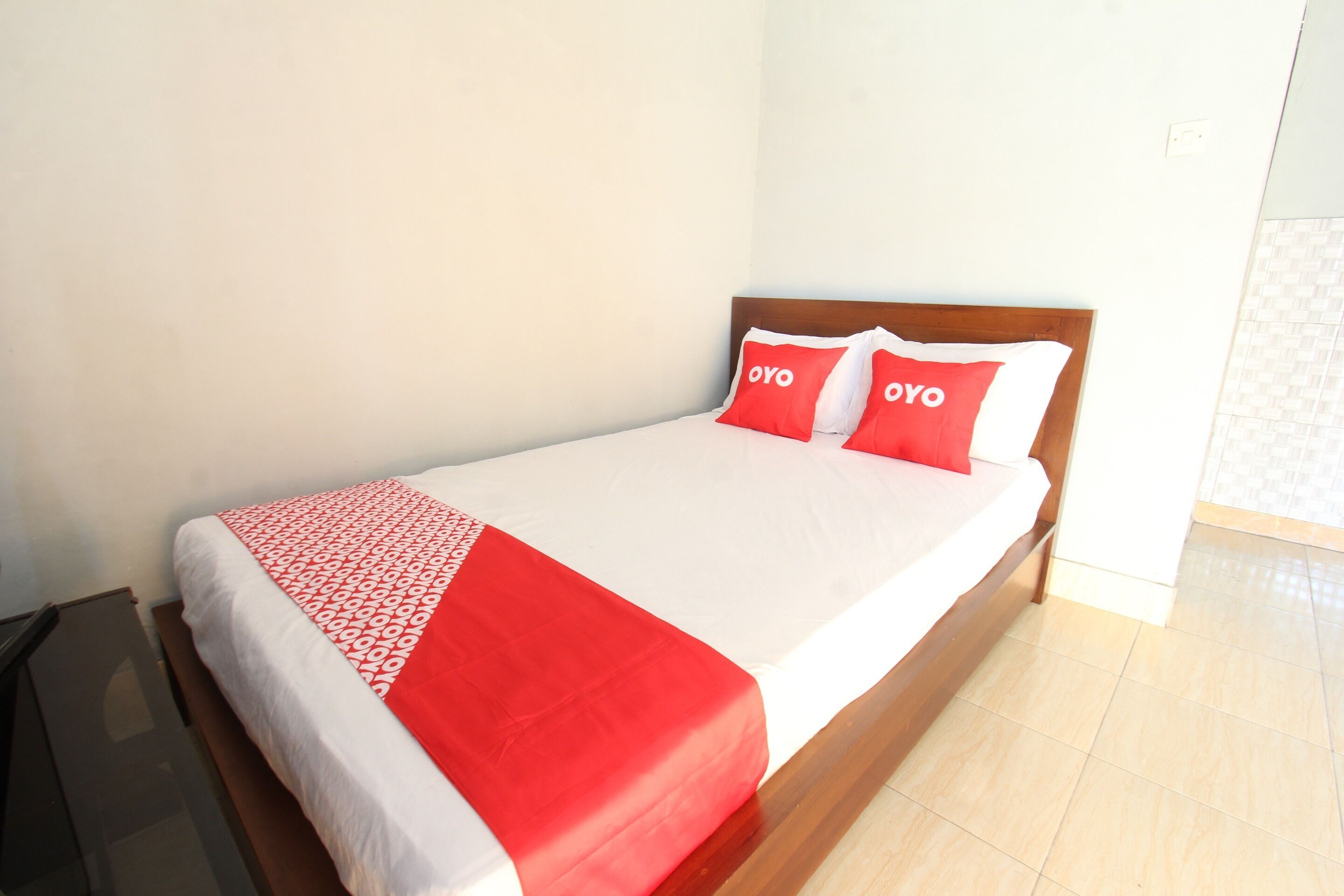 A bed with a white and red bedspread, two red pillows with "OYO" text, and a wooden headboard.