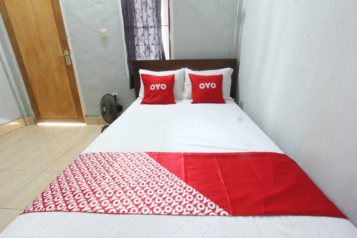 Un lit avec deux oreillers rouges portant l’inscription « OYO », un couvre-lit blanc et une couverture à motifs rouges et blancs.