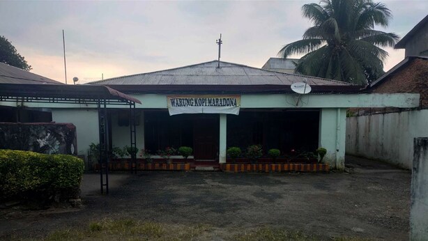Un bâtiment sur lequel on peut lire l’inscription « WARUNG KOPI MARADONA » et qui est surmonté d’une antenne parabolique.