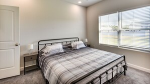 A bedroom with a bed, bedside tables, a nightstand, a window with blinds, and a door. - Cape Charles Home: 4 Mi to Kiptopeke State Park! (Cape Charles)