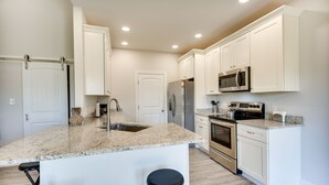 A modern kitchen with white cabinets, granite countertops, stainless steel appliances, and a central island with stools. - Cape Charles Home: 4 Mi to Kiptopeke State Park! (Cape Charles)