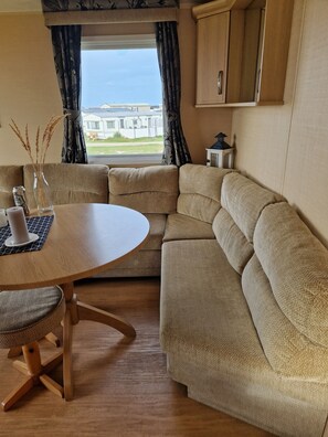 A cozy living area with a round wooden table, beige sofa, and a window with curtains. - Schön Gelegenes Chalet in Einer Dünenlandschaft (Ballum)