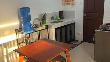 Uma cozinha compacta com mesa e cadeiras, dispenser de água e fogão.