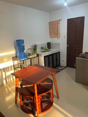 Een kleine keuken met een eettafel en stoelen, een waterdispenser en een fornuis.
