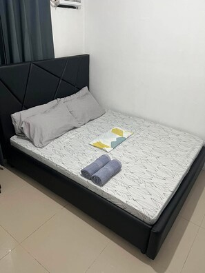 A single bed with a black headboard, a patterned mattress, two pillows, and two rolled towels. - Vin's Place Tagum City (Tagum)
