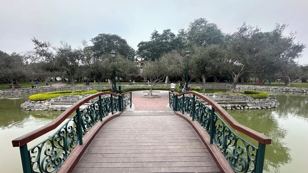 A wooden bridge with ornate metal railings leading to a pond surrounded by trees. -  Aparts4Days 1 Bedroom Apartment San Isidro Olivar (Lima)
