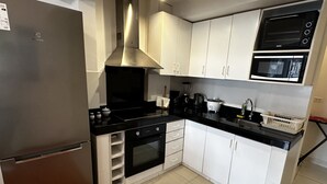 A compact kitchen with a stainless steel refrigerator, a built-in oven, a microwave, and white cabinetry. -  Aparts4Days 1 Bedroom Apartment San Isidro Olivar (Lima)