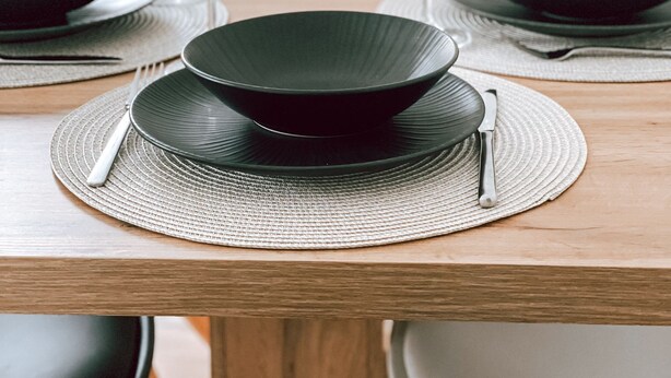 A dining table set with black plates, clear wine glasses, and silverware on woven placemats. - Stilvolles Gemütliches Modernes Haus 4-7 Person - Netflix - Wlan (Passau)