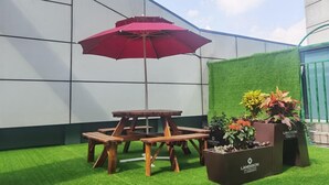 En terrasse med et træbord og bænke, en rød parasol og plantekrukker.