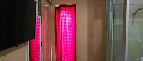 A narrow hallway with a tiled floor, a red curtain, a mounted air conditioner, and a glass shower enclosure.