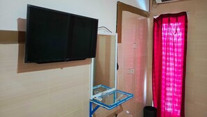 Quarto com televisão montada na parede, uma mesa pequena com tampo de vidro, cortina vermelha e unidade de ar condicionado.