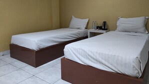 Quarto de hotel com duas camas de solteiro, uma mesinha com chaleira e uma tomada na parede.