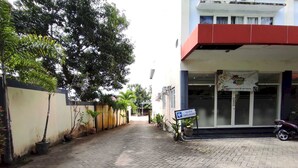 Uma trilha pavimentada conduz a um edifício com uma placa indicando 'PARKIR DIBELAKANG'.
