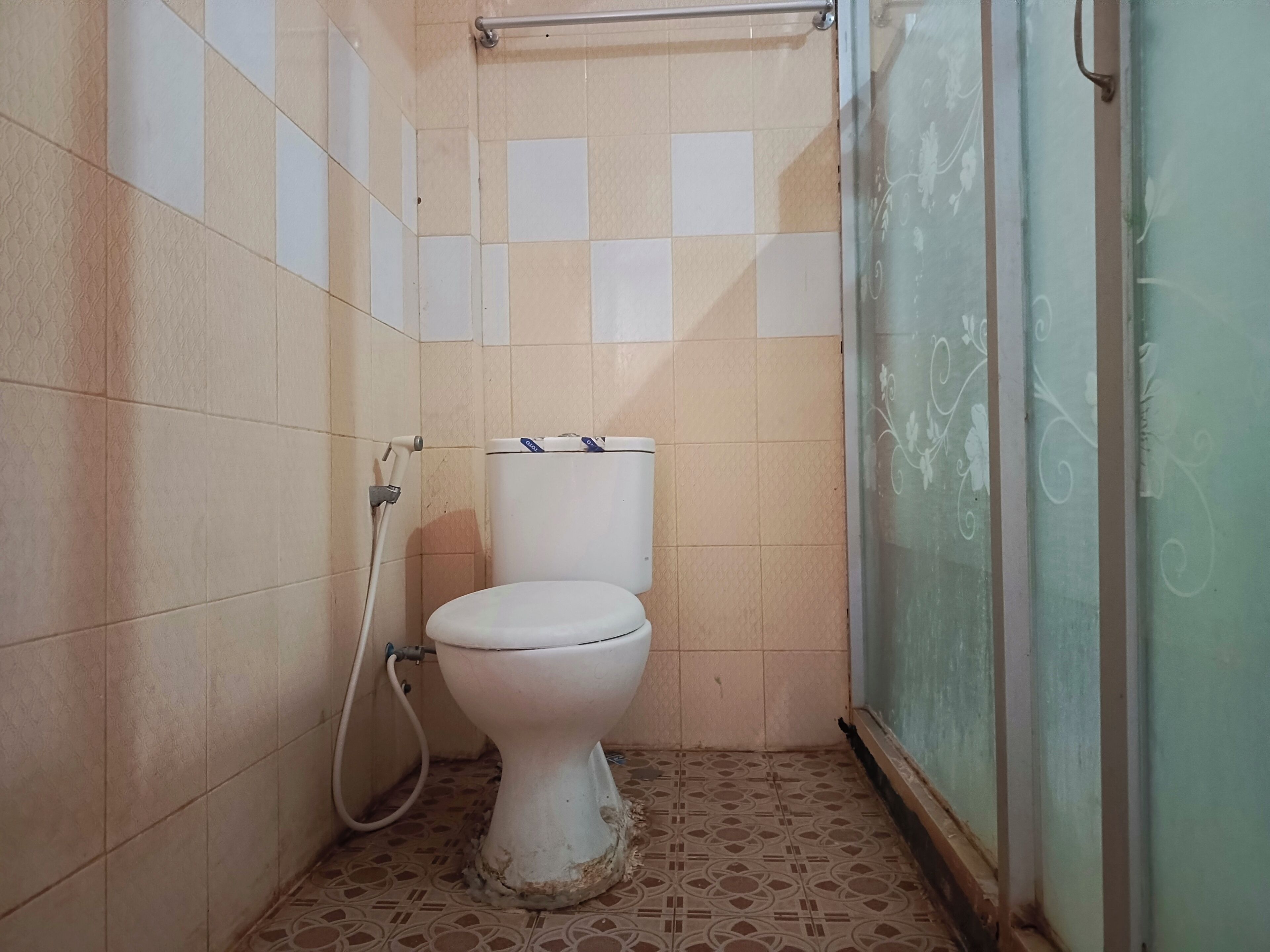 Et lille badeværelse med fliser, toilet, bruseniche og en glasdør.