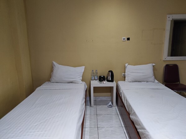 A hotel room with two single beds, a small table with a kettle, a phone, and bottled water.