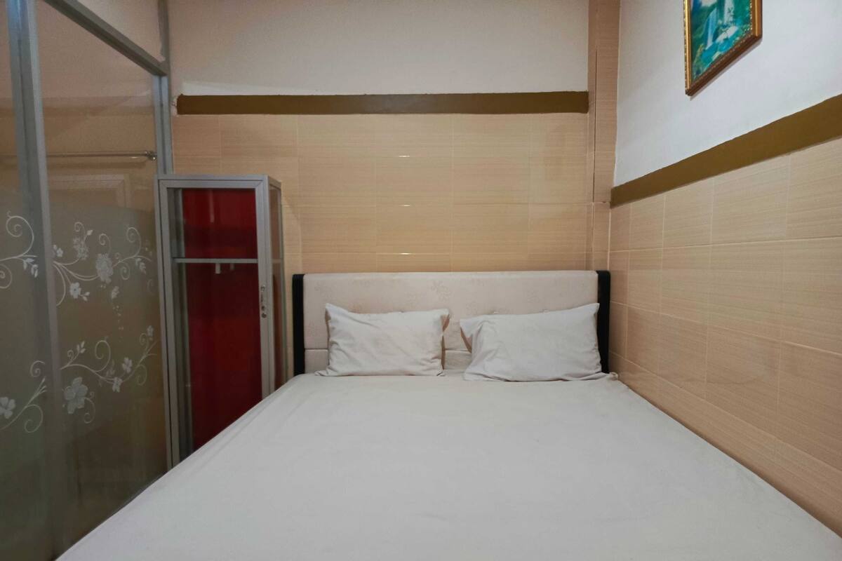 A single bed with white bedding in a room with beige walls and a wooden headboard.