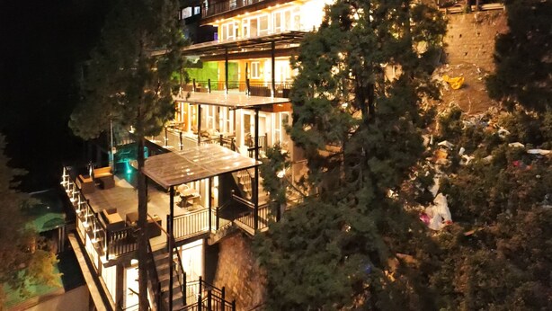 A multi-story building with balconies and outdoor seating areas, surrounded by trees. - Hotel Rex  (Dehradun)