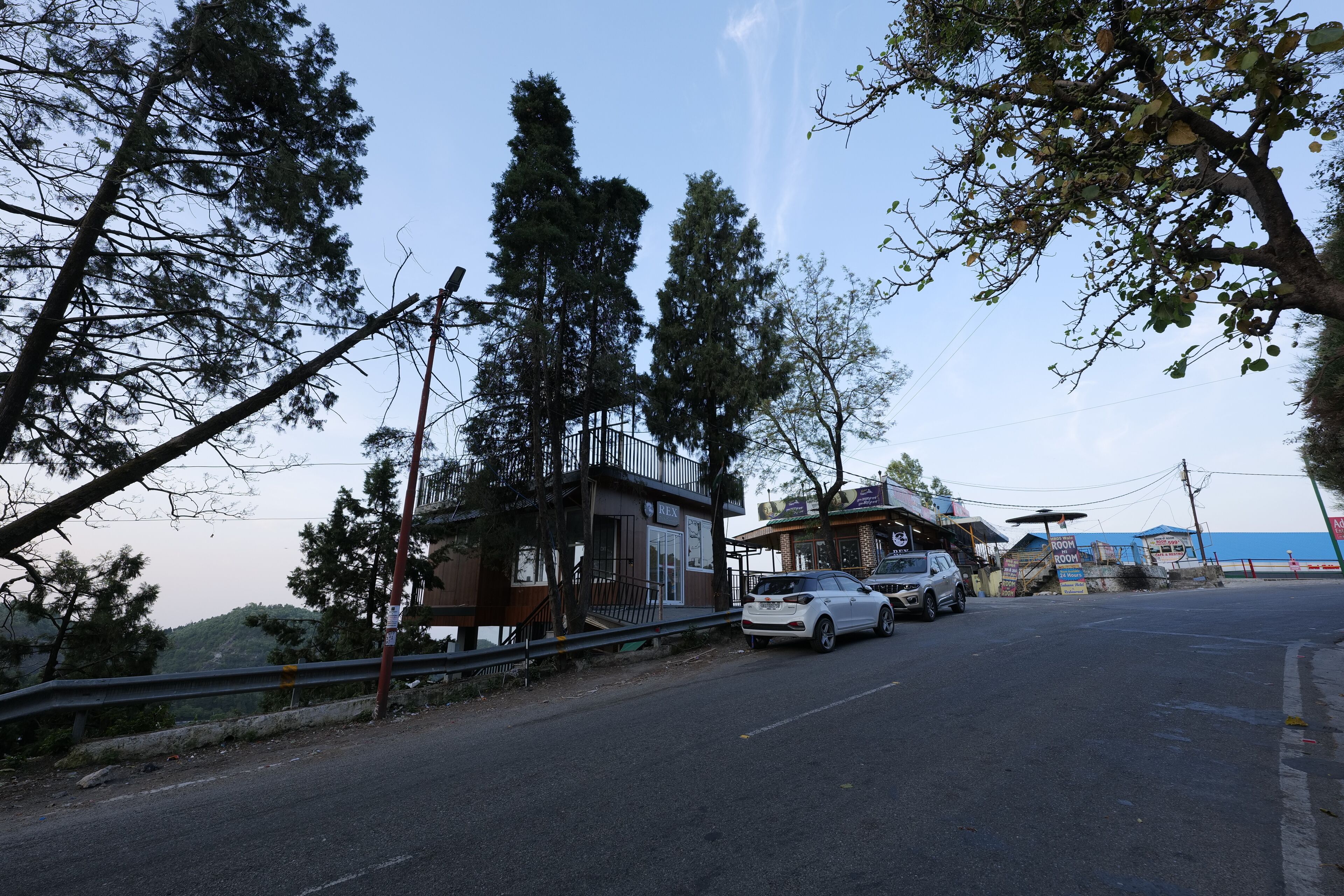 A road with parked cars, a building with a sign 'ROOM', and trees.