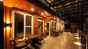A covered outdoor seating area with tables and chairs, wooden paneling, and a staircase leading to an upper level. - Hotel Rex  (Dehradun)