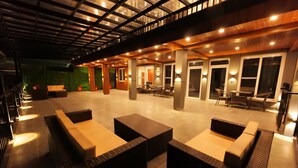 An outdoor lounge area with wicker furniture, ambient lighting, and a covered section with a wooden ceiling. - Hotel Rex  (Dehradun)