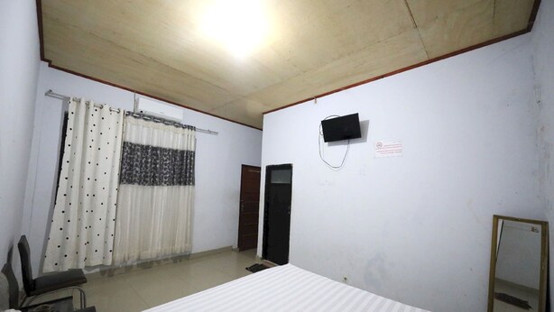 A room with a bed, a chair, a television mounted on the wall, and a mirror. - Hotel O Kos Citra Syariah Near Bukit Marezo (Makassar)