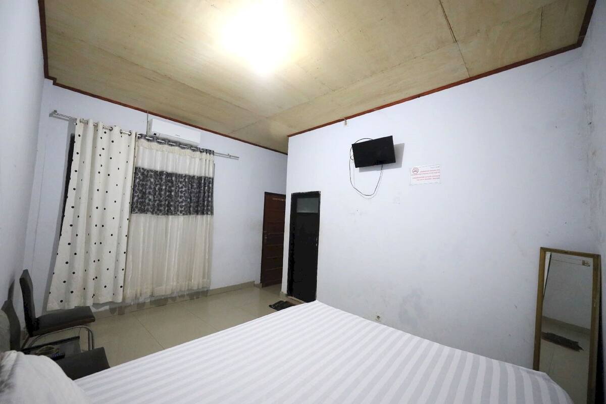 A room with a bed, a chair, a television mounted on the wall, and a mirror.
