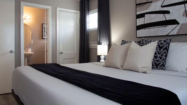 Een hotelkamer met een groot bed, een badkamer met een spiegel en wastafel, en een schilderij aan de muur.