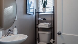 Een badkamer met een witte wastafel, een spiegel, een toilet, een plank met handdoeken en een kamerplant.